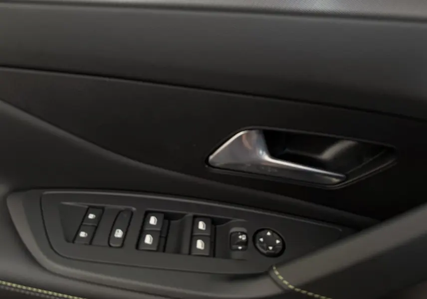 Détail intérieur montrant la commande des vitres et la poignée de porte côté conducteur d’une Peugeot 308 Hybrid 2024 gris foncé.