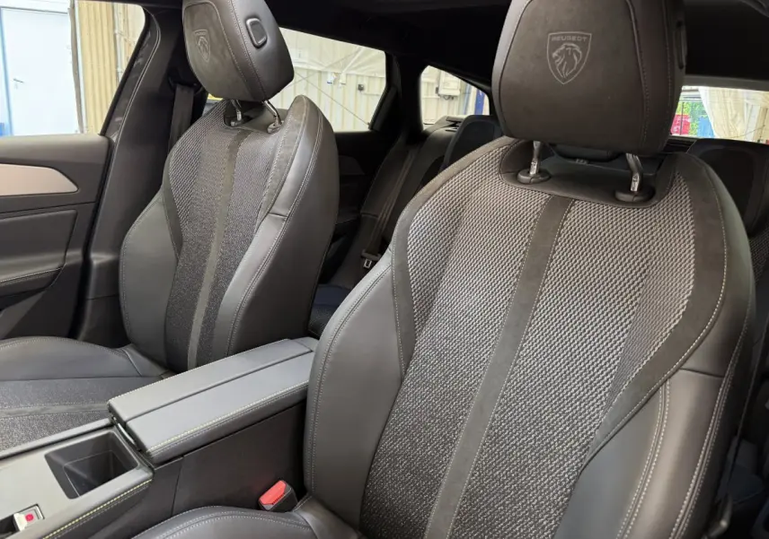 Gros plan sur les sièges avant gris foncé en cuir et tissu du Peugeot 308 Hybrid 2024 avec logo Peugeot brodé sur les appuie-têtes.