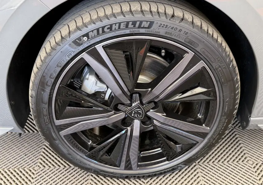 Gros plan sur la roue avant droite d’une Peugeot 308 Hybrid 136 e-DCS6 GT gris foncé avec jante noire brillante et pneu Michelin.