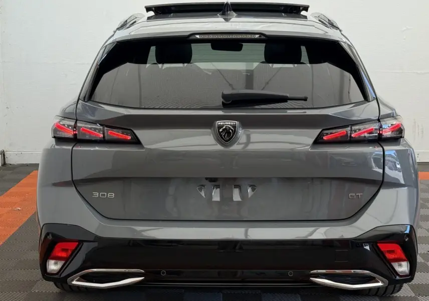 Vue arrière d’une Peugeot 308 GT gris foncé avec feux LED allumés et double sortie d’échappement chromée.