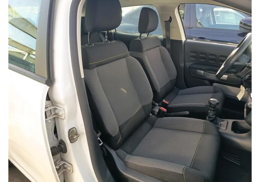 Vue intérieure côté conducteur d'une Citroën C3 blanche 2021, montrant les sièges avant en tissu gris avec surpiqûres jaunes.