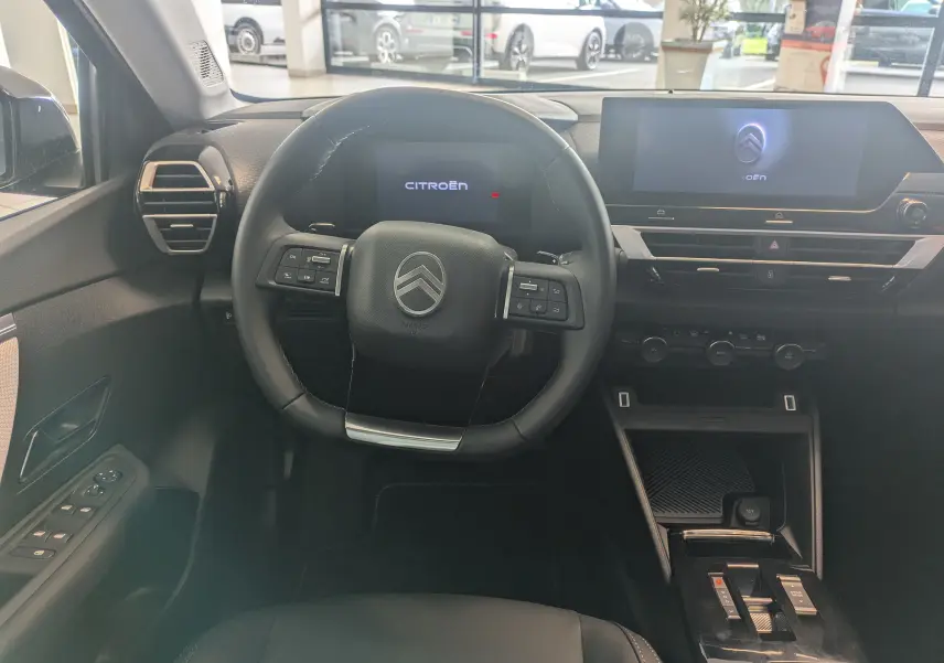 Vue intérieure centrée sur le volant noir et l’écran tactile du tableau de bord de la Citroën C4 hybride 2025.