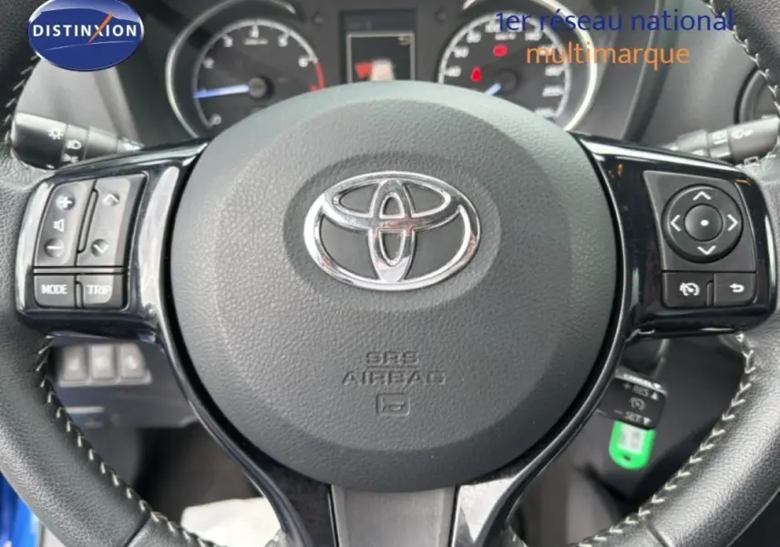 Gros plan sur le volant multifonctions en cuir noir de la Toyota Yaris bleu foncé, avec commandes intégrées et logo central.