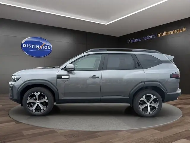 Vue de profil côté gauche du SUV Dacia Bigster gris foncé, avec roues alliage et barres de toit noires visibles.