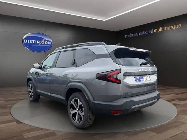 Vue 3/4 arrière droite du Dacia Bigster gris foncé avec toit noir et jantes alliage distinctives dans un showroom.