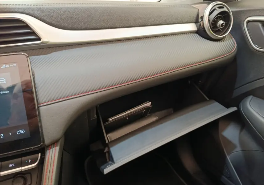 Vue rapprochée de la boîte à gants ouverte côté passager du tableau de bord noir avec surpiqûres rouges du MG ZS Luxury 2024.