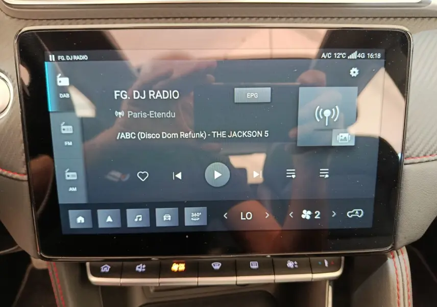 Écran tactile central du MG ZS Luxury 2024 affichant la radio et commandes climatisation, intérieur noir avec surpiqûres rouges.