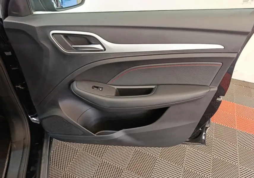 Gros plan sur la porte avant gauche noire du MG ZS Luxury 70kWh 2024, avec poignée et habillage intérieur noir et surpiqûres rouges.