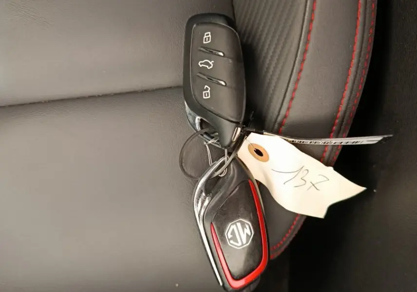 Clé de voiture MG Motor ZS Luxury noire posée sur siège cuir noir avec surpiqûres rouges, vue rapprochée.