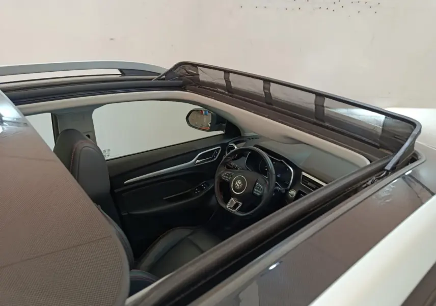 Vue intérieure par le toit ouvrant du MG Motor ZS Luxury 70kWh 2024 noir, volant cuir multifonctions et sièges noirs.