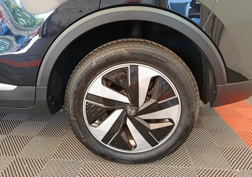 Gros plan sur la roue avant droite noire du MG ZS Luxury 2024 avec jante bicolore et logo MG au centre.