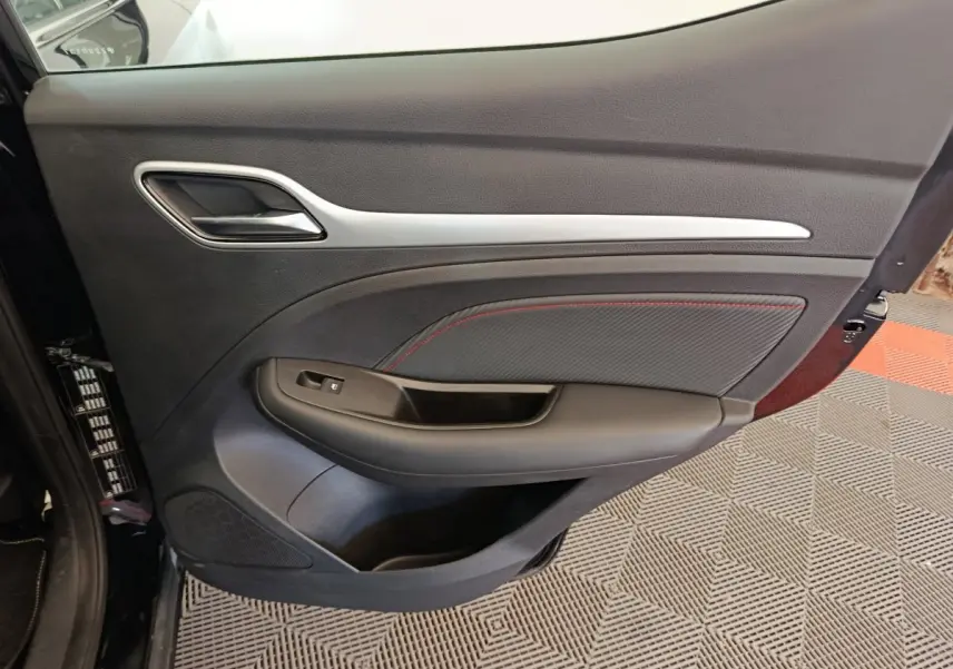Vue intérieure du panneau de porte avant gauche noir avec surpiqûres rouges du MG ZS Luxury 2024 électrique.