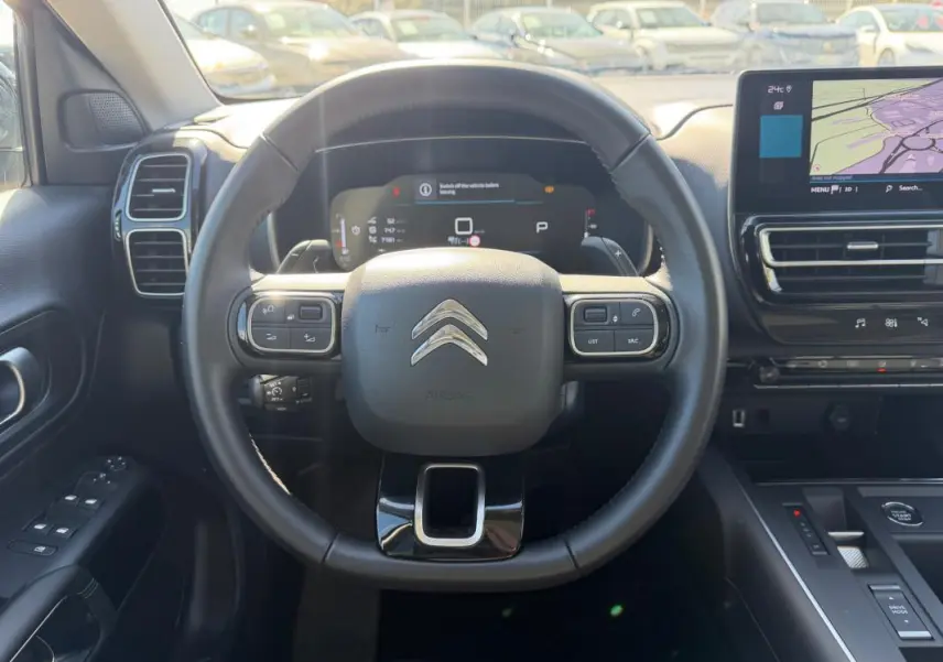 Vue intérieure centrée sur le volant noir du Citroën C5 Aircross 2024 hybride avec tableau de bord numérique et écran tactile.