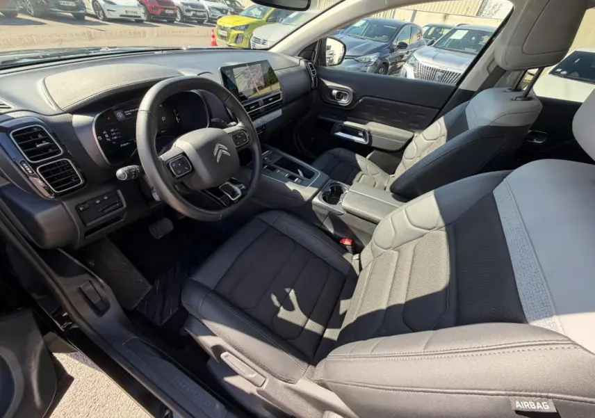 Vue intérieure côté conducteur du Citroën C5 Aircross Hybride 2024 noir, avec tableau de bord et sièges en tissu gris.