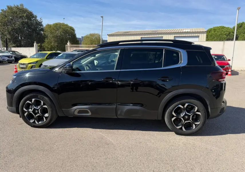 Vue de profil côté gauche d'un Citroën C5 Aircross hybride noir 2024 avec jantes distinctives et barres de toit.