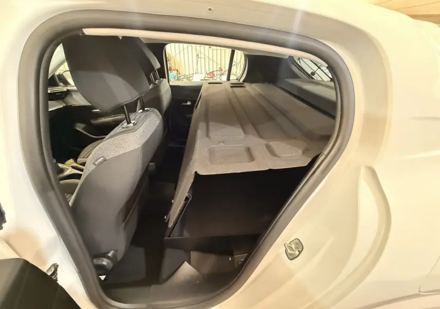 Vue intérieure côté droit de la Peugeot 208 blanche, montrant la banquette arrière avec cache-bagages relevé.
