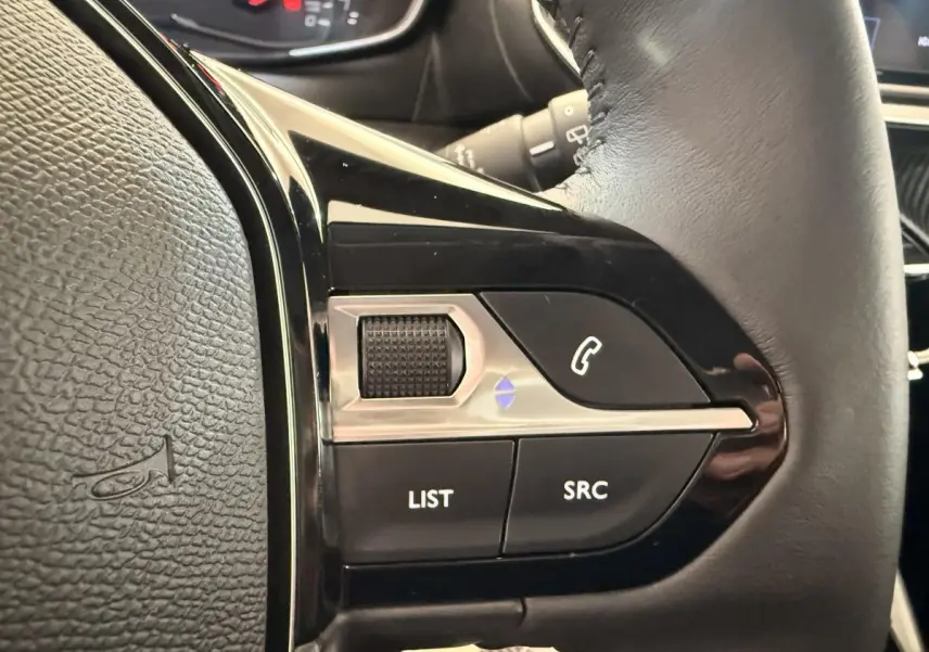 Gros plan sur les commandes multifonctions côté gauche du volant cuir noir d’une Peugeot 208 blanche de 2025.