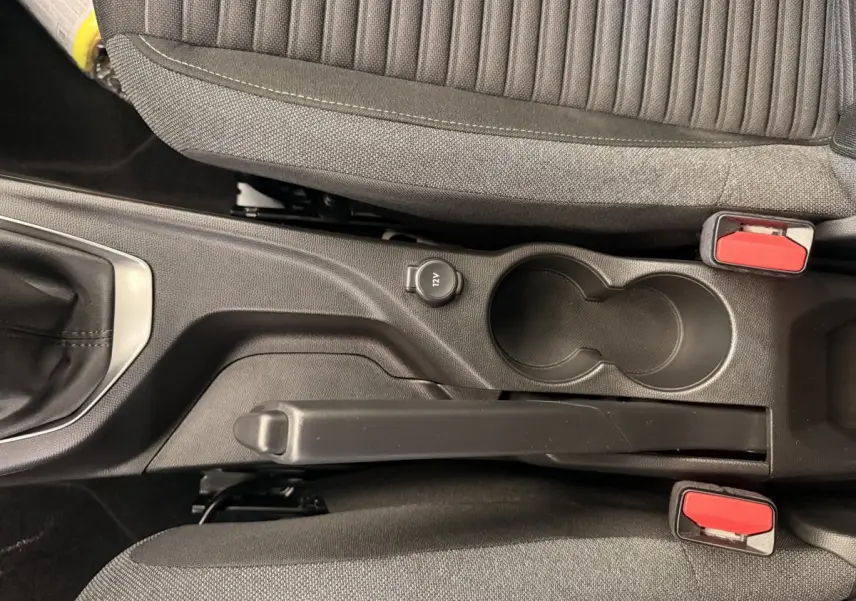 Vue plongeante sur la console centrale noire de la Peugeot 208 blanche, avec frein à main manuel et prise 12V visible.