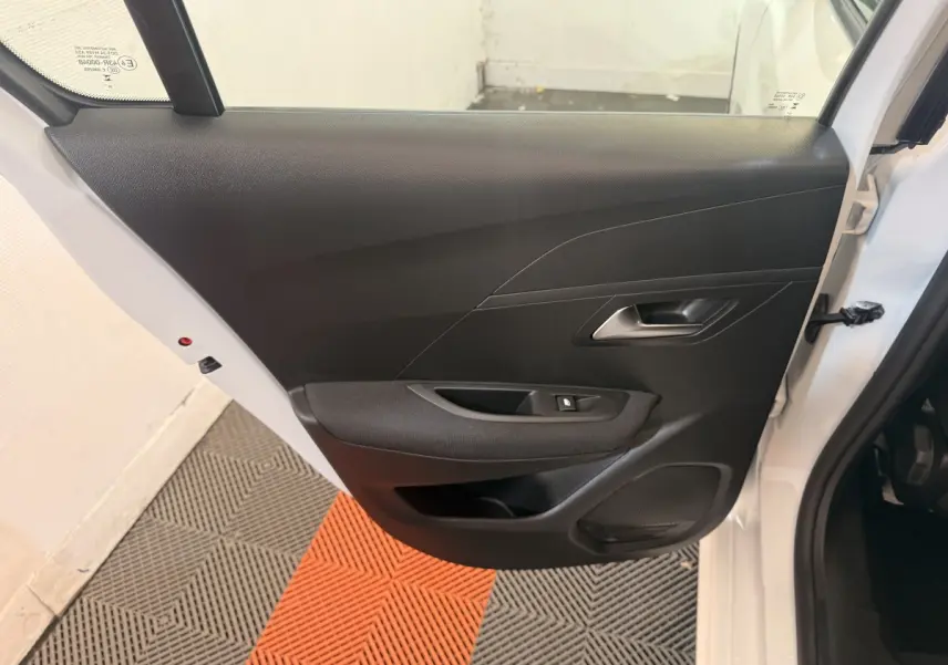 Vue intérieure de la porte arrière gauche d'une Peugeot 208 blanche, avec panneau noir et commande de vitre électrique.