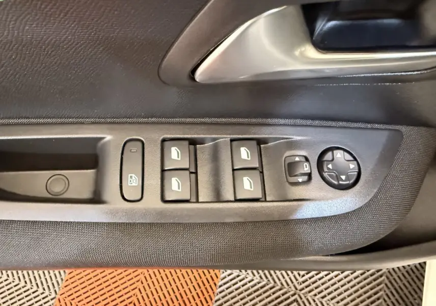 Gros plan sur les commandes des vitres et rétroviseurs côté conducteur d'une Peugeot 208 blanche.