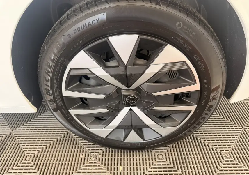 Gros plan sur la roue avant droite blanche de la Peugeot 208 avec jante en alliage noir et argent au design géométrique.