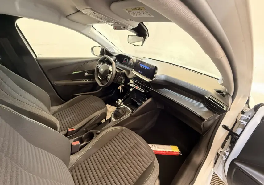 Intérieur de la Peugeot 208 blanche vue côté conducteur, montrant sièges noirs, volant cuir et écran tactile central.