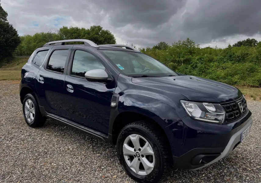 Dacia Duster 1.5 DCI bleu marine vu de 3/4 avant droit, avec barres de toit argentées et jantes alliage.