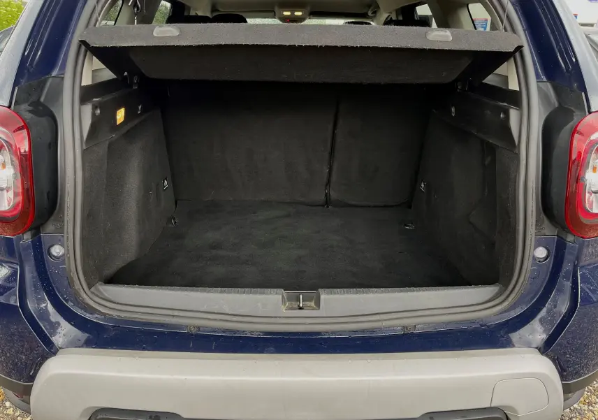 Coffre ouvert d'un Dacia Duster bleu marine 2018 vu de l'arrière, montrant un espace de chargement vide et propre.