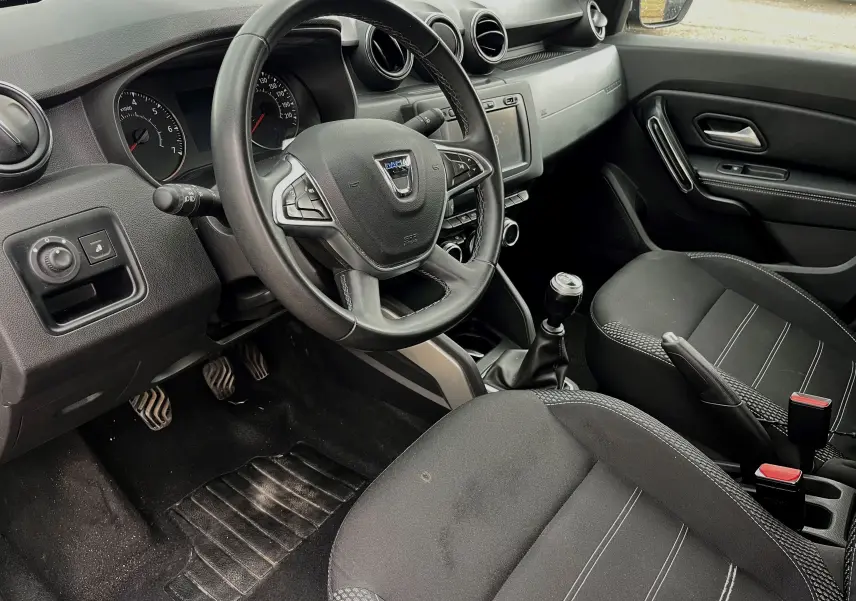 Intérieur du Dacia Duster 1.5 DCI 2018 vu côté conducteur, volant multifonction et sièges noirs avec surpiqûres grises.
