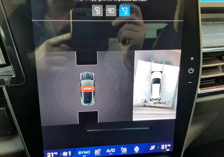 Écran tactile du Renault Austral E-Tech Hybrid montrant la caméra de recul avec vue aérienne du véhicule blanc nacré toit noir.
