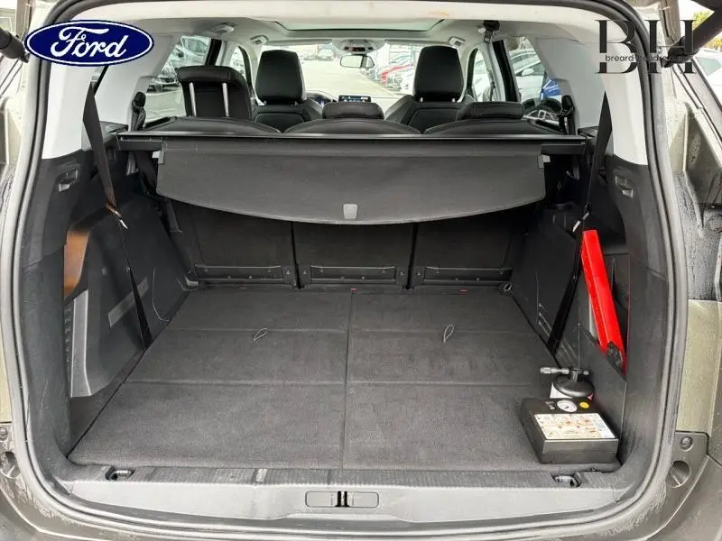 Coffre ouvert vu de l'arrière d'un SUV gris avec banquette arrière rabattue et cache-bagages déployé.