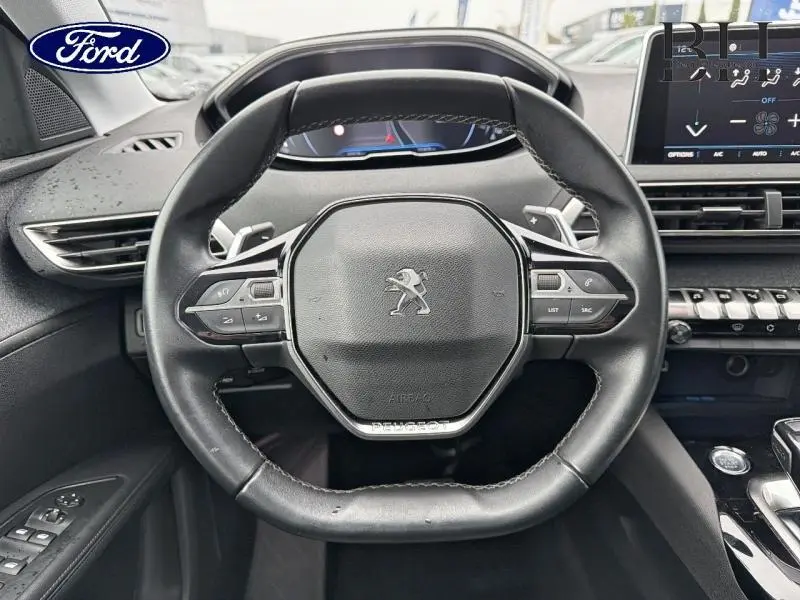 Vue rapprochée du volant cuir multifonction noir du Peugeot 5008 avec tableau de bord numérique et écran tactile à droite.