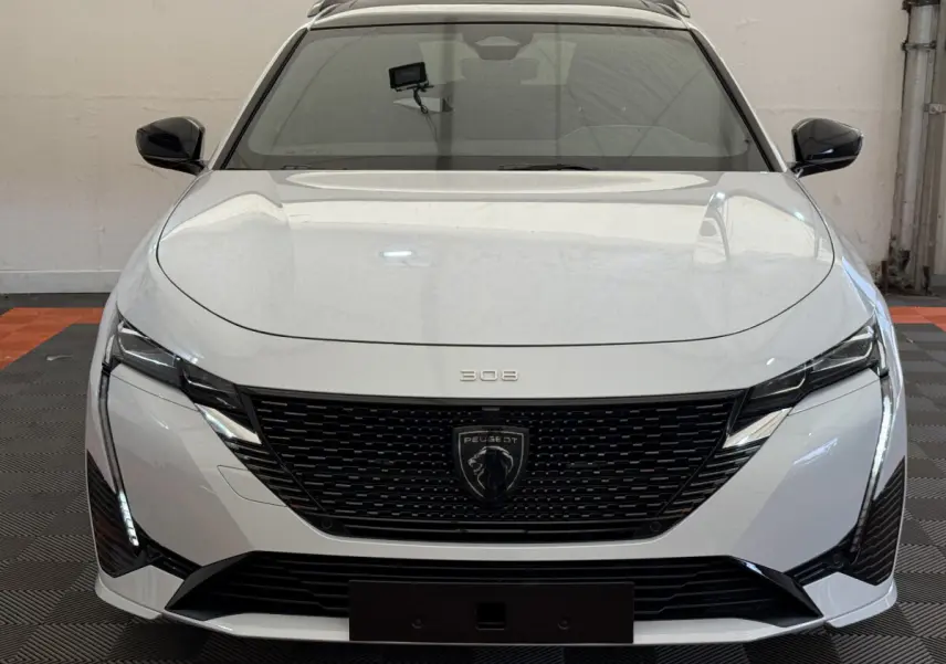 Vue frontale d'une Peugeot 308 Hybrid 136 e-DCS6 GT blanche avec calandre noire et feux LED verticaux.