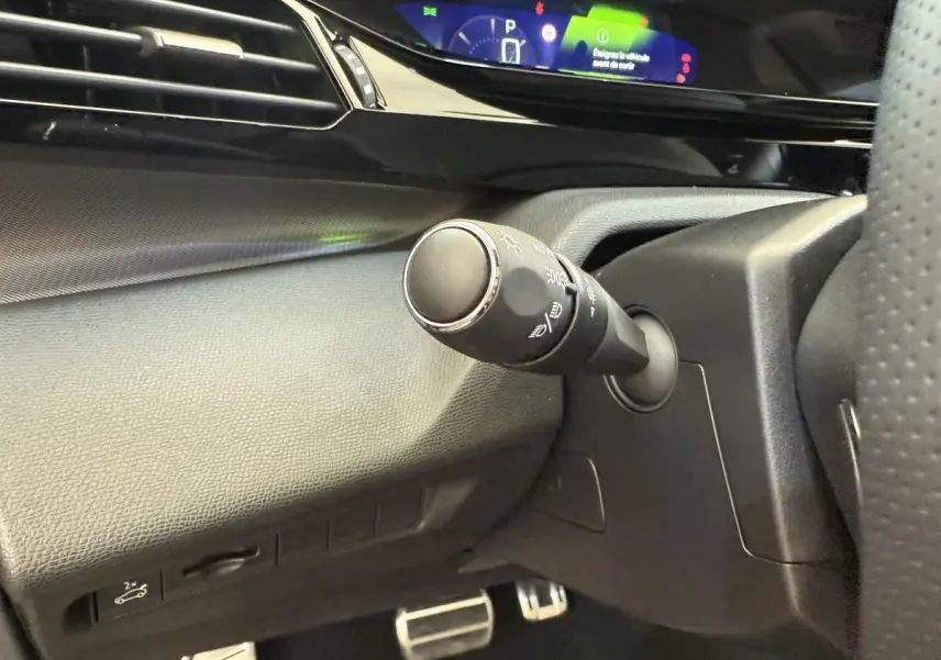 Gros plan sur la commande d’éclairage à gauche du volant dans l’habitacle noir du Peugeot 308 Hybrid 136 e-DCS6 GT 2024.