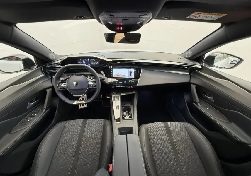 Vue intérieure avant de la Peugeot 308 Hybrid 136 e-DCS6 GT 2024, tableau de bord moderne avec écran tactile central et volant cuir noir.