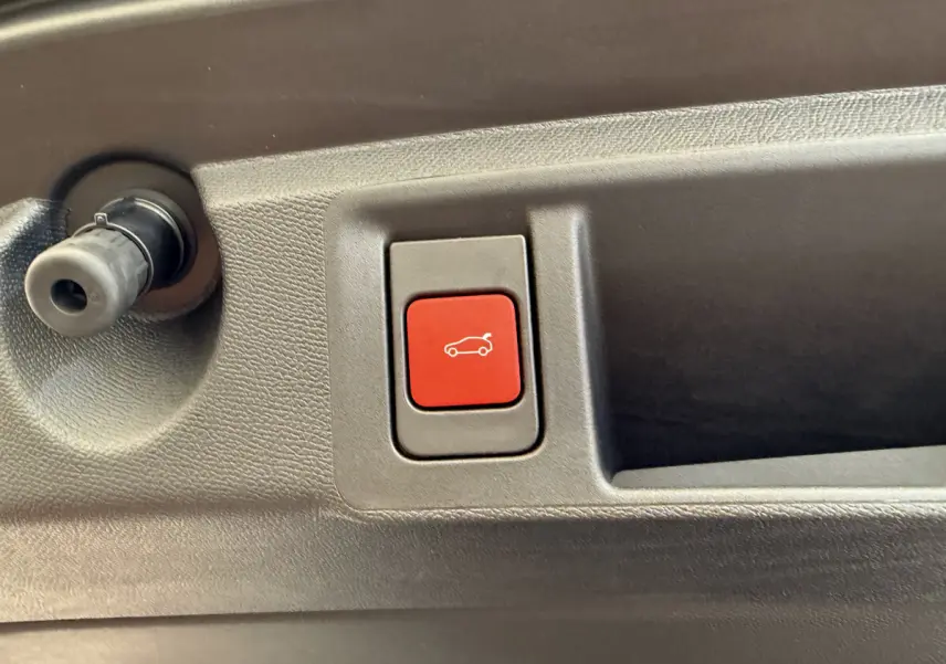 Gros plan sur le bouton rouge d'ouverture électrique du coffre dans l'habitacle d'une Peugeot 308 Hybrid 2024.