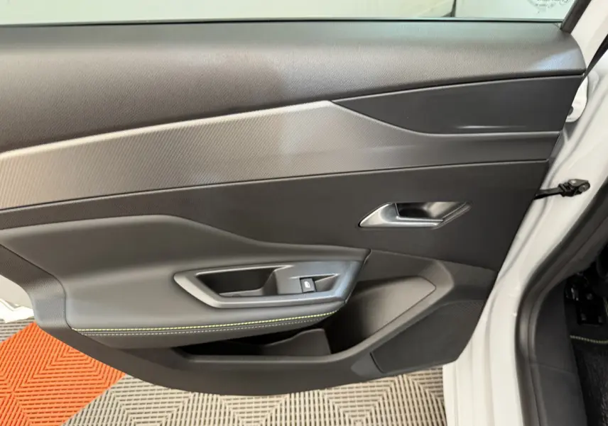 Vue intérieure de la porte avant droite blanche de la Peugeot 308 Hybrid 136 e-DCS6 GT avec garniture noire et surpiqûres vertes.