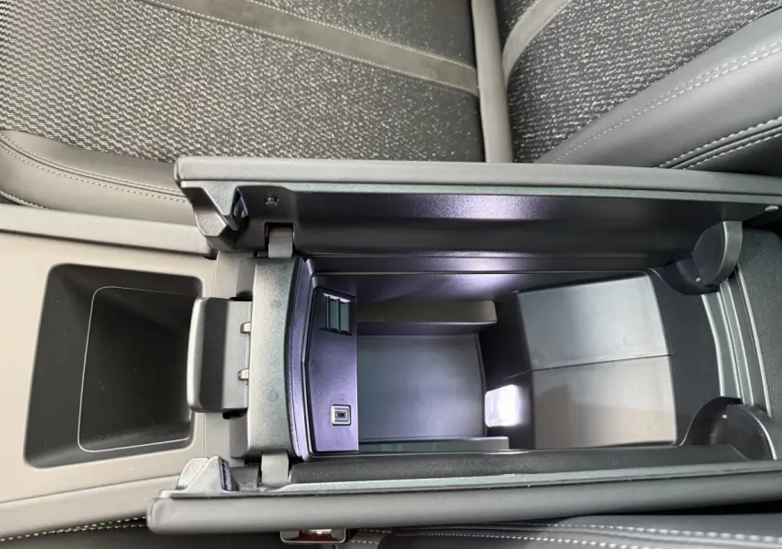 Vue rapprochée de l'accoudoir central ouvert avec compartiment de rangement et port USB dans l'habitacle du Peugeot 308 Hybrid blanc.
