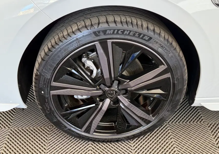 Gros plan sur la roue avant gauche de la Peugeot 308 Hybrid blanche, mettant en valeur la jante noire et argentée au design moderne.