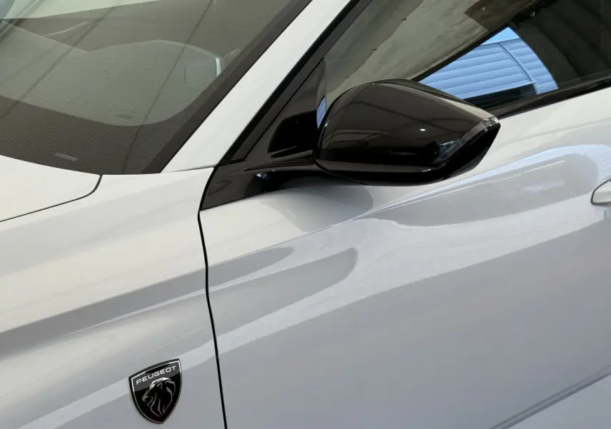 Détail du côté gauche blanc d’une Peugeot 308 Hybrid 136 e-DCS6 GT avec rétroviseur noir brillant et logo Peugeot.