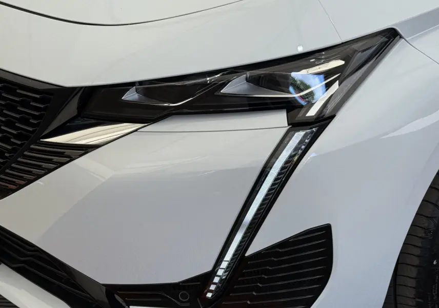 Gros plan sur le phare avant droit blanc du Peugeot 308 Hybrid 136 e-DCS6 GT avec éclairage LED distinctif en forme de griffes.
