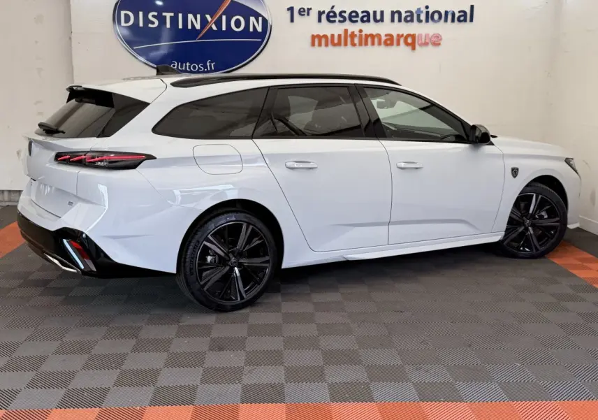 Peugeot 308 Hybrid 136 GT blanc vue de profil droit, jantes noires et toit noir contrasté en intérieur showroom.