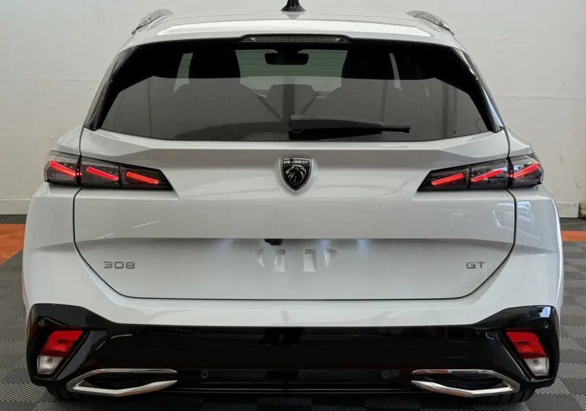 Vue arrière d’une Peugeot 308 GT blanche 2024 avec feux LED allumés et double sortie d’échappement chromée.