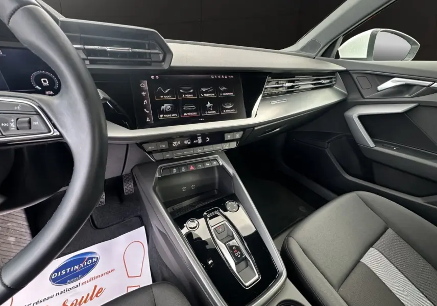 Vue intérieure côté conducteur de l’Audi A3 2024 blanche, mettant en valeur la console centrale moderne et l’écran tactile.