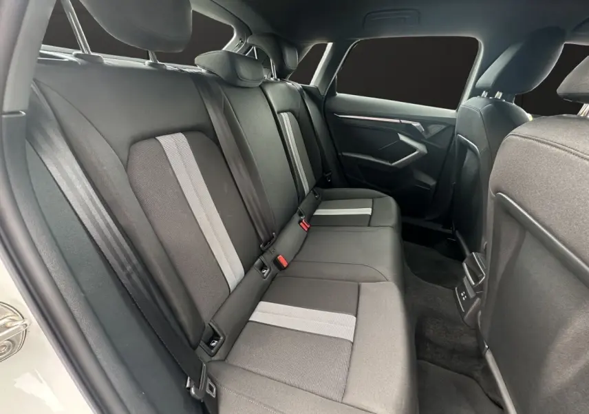 Vue intérieure arrière côté gauche de l'Audi A3 blanc 2024, montrant les sièges arrière en tissu avec bandes grises.