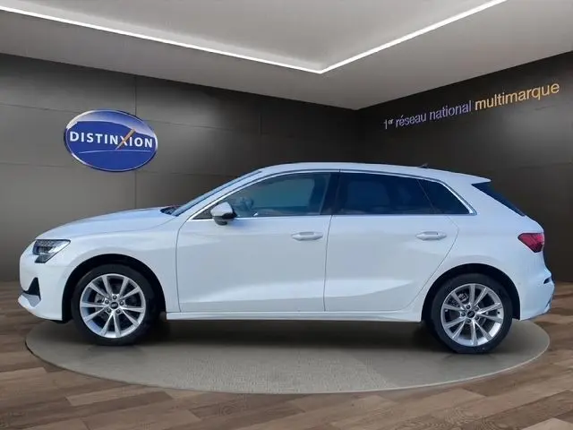 Audi A3 30 TFSI blanc vue de profil côté gauche, sur plateforme en showroom avec logo Distinxion en arrière-plan.