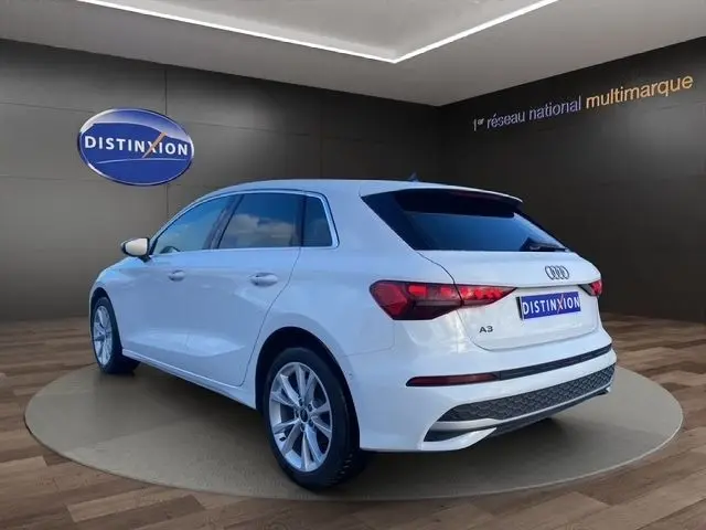 Vue 3/4 arrière droite de l'Audi A3 30 TFSI blanche en finition Advanced Edition, dans un showroom Distinxion.
