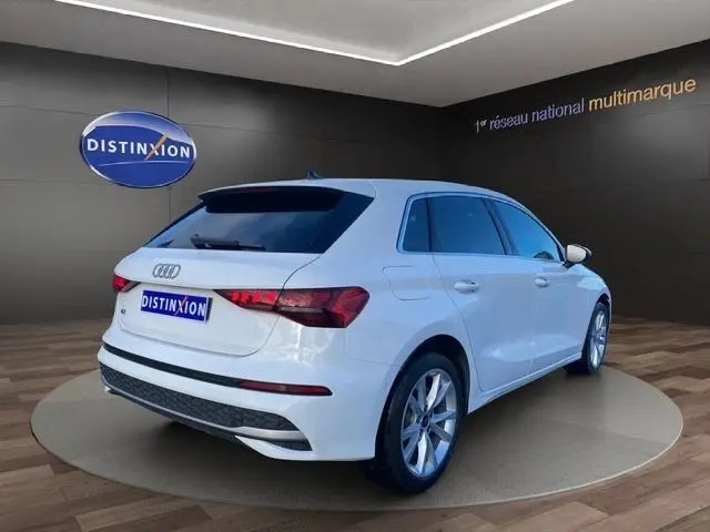 Vue 3/4 arrière droite d'une Audi A3 blanche 2024, version 30 TFSI MHEV, avec jantes alliage et feux LED distinctifs.