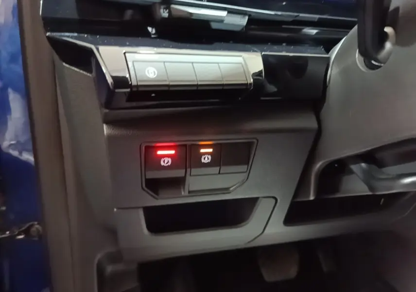 Détail intérieur côté gauche du tableau de bord du Renault Austral bleu, avec boutons de frein à main électrique éclairés.