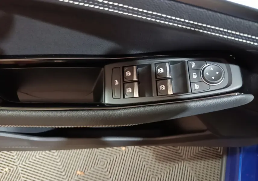 Gros plan sur les commandes de lève-vitres et rétroviseurs sur la porte côté conducteur d’un Renault Austral bleu 2024.